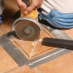 With both hands firmly holding the grinder, the author carefully plunges the blade into the tile’s center and cuts diagonally, then along the tile’s sides.