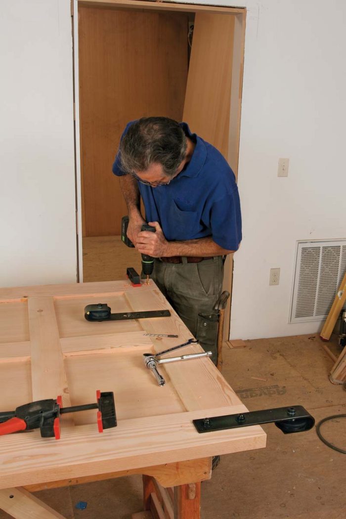 Next, shim it plumb, and place the rollers on the track. Center the mounting brackets in the door’s stiles, and trace the screw holes for drilling.