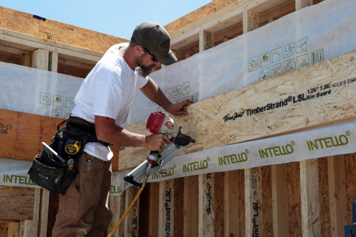 A splice of Intello is tacked in place before Mike uses the MAX framing nailer to hang the rim board for the second floor system. The strip of membrane ensures a continuous air barrier after framing is complete.