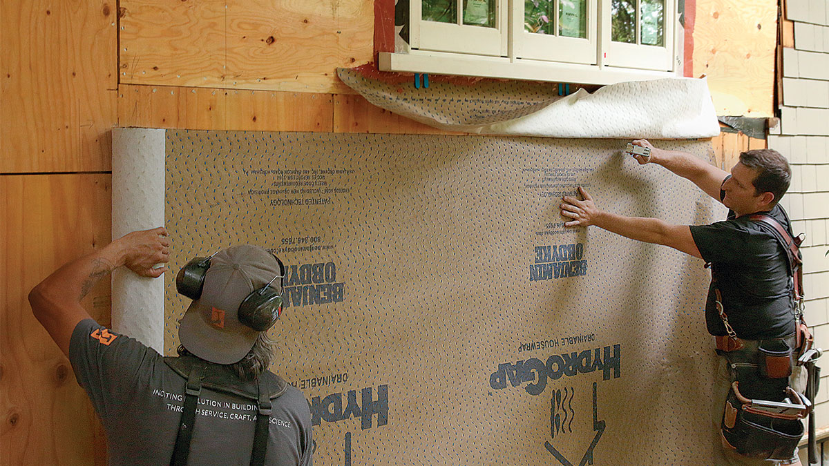 Two people working on the wall of a home 