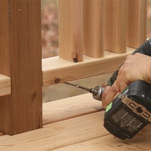 Fasten the bottom. After removing the blocks spacing the rail off the deck surface, drive the lower screws. The clearance is tight, but a right-angle drill attachment helps to set them.