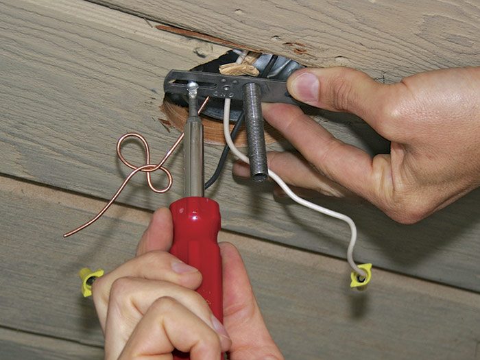 Screwing a mounting bracket with a threaded nipple to a ceiling box.