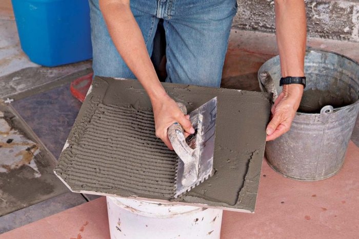 Comb an even layer of thinset onto the back of the cut tiles with a notched trowel.