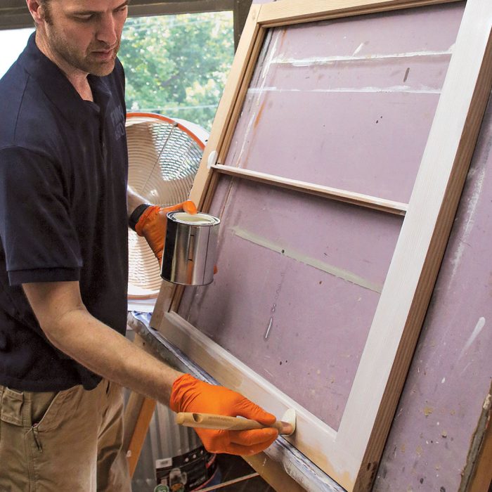 Photo of a man wearing orange gloves painting a window frame with linseed oil paint.