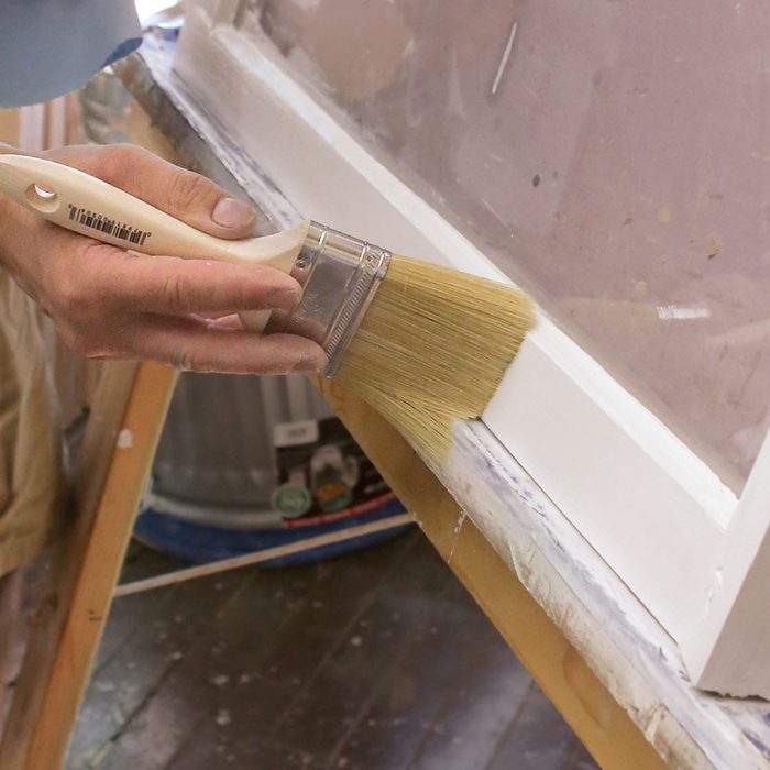 Photo of a hand brushing a final coat of linseed oil paint to a window frame.