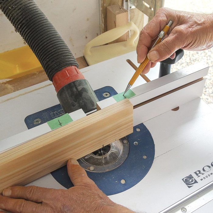 Photo of hands markings the fence on a piece of wood on the router table.