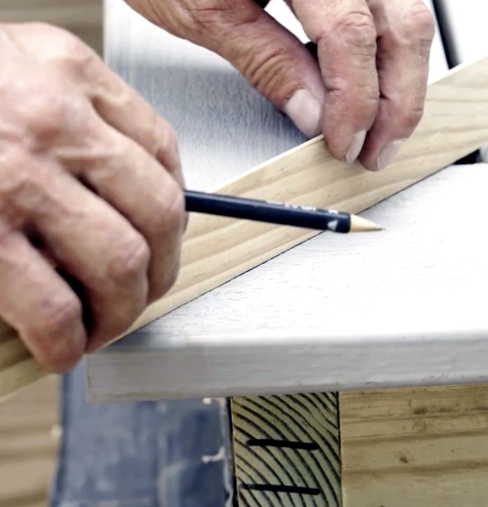 Photo of two hands using a small piece of wood to measure the space between deck boards.